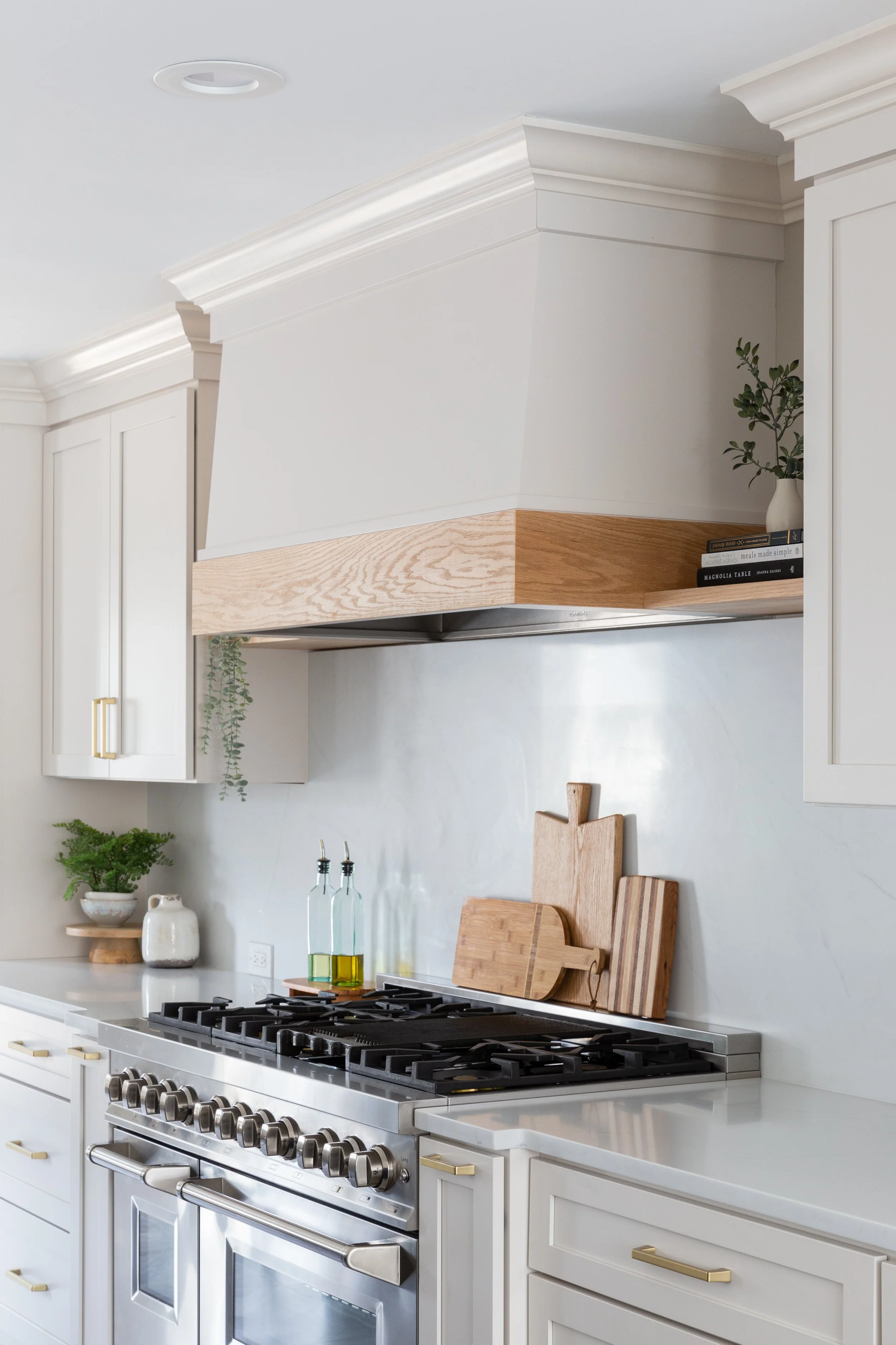 Modern kitchen with white cabinets, a stainless steel oven and stove, wooden cutting boards, a potted plant, and glass bottles with oil on the countertop.