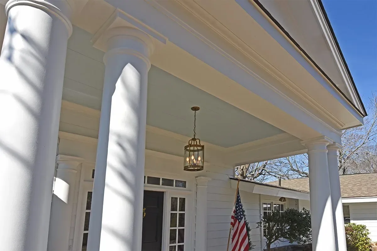 Renovated front porch featuring white columns, detailed trim, a covered entry, and a statement pendant light.