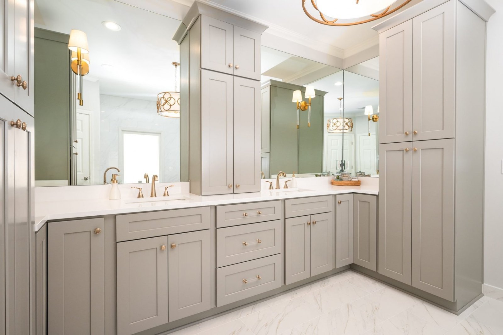 The oversized double vanity includes custom shaker-style cabinetry, quartz countertops, brushed brass hardware, and expansive mirrors designed to maximize both storage and functionality.