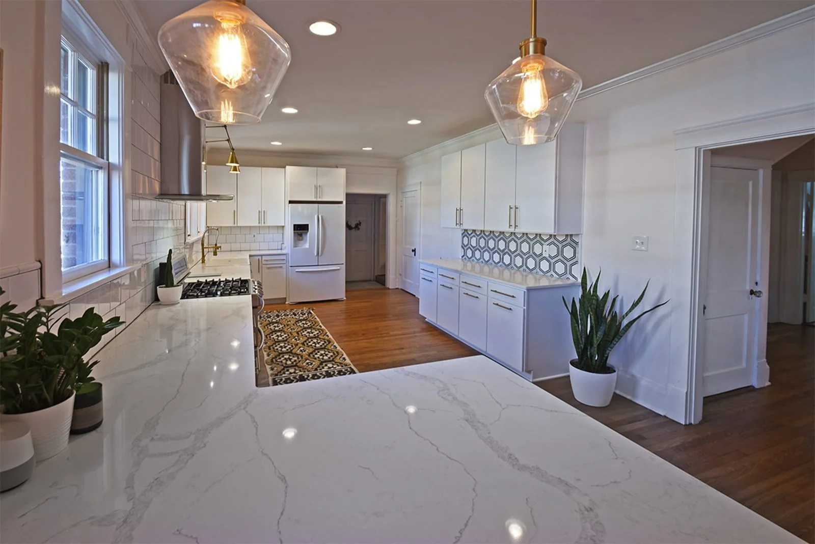Modern white kitchen remodel with quartz countertops, custom cabinetry, pendant lighting, and hardwood floors in Germantown, TN.