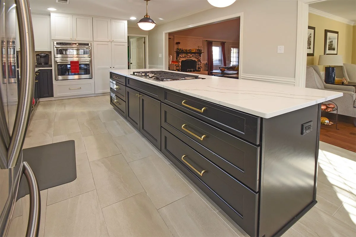 Modern kitchen with black and white cabinets, white marble island, stainless steel appliances, and beige tiled floor.