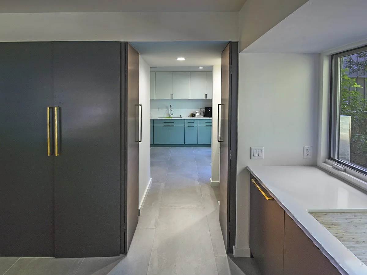 View into a modern kitchen through a doorway, with cabinets, a window, and a countertop.