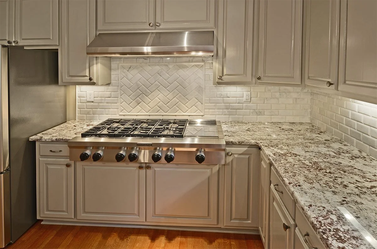 Kitchen with gray cabinets, granite countertops, white subway tile backsplash, stainless steel stovetop, and stainless steel hood vent