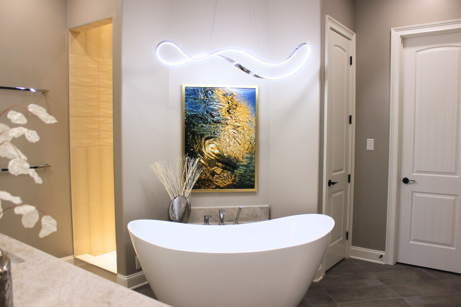A sculptural LED pendant light and freestanding soaking tub serve as the focal point of this modern primary bathroom remodel in Duncan Woods, blending contemporary style with spa-inspired comfort.