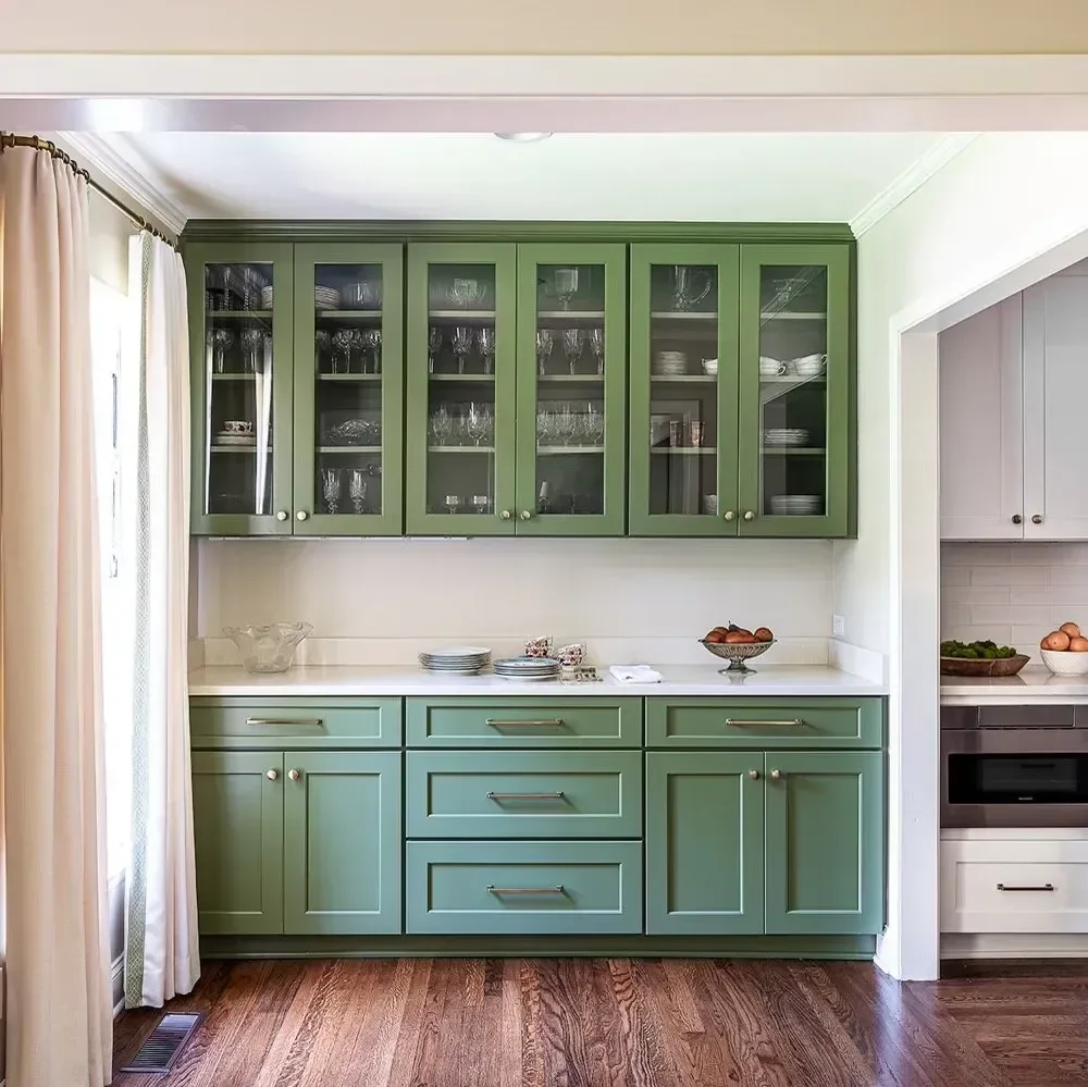 Kitchen with green cabinets and glass-front upper cabinets displaying glassware and dishes.