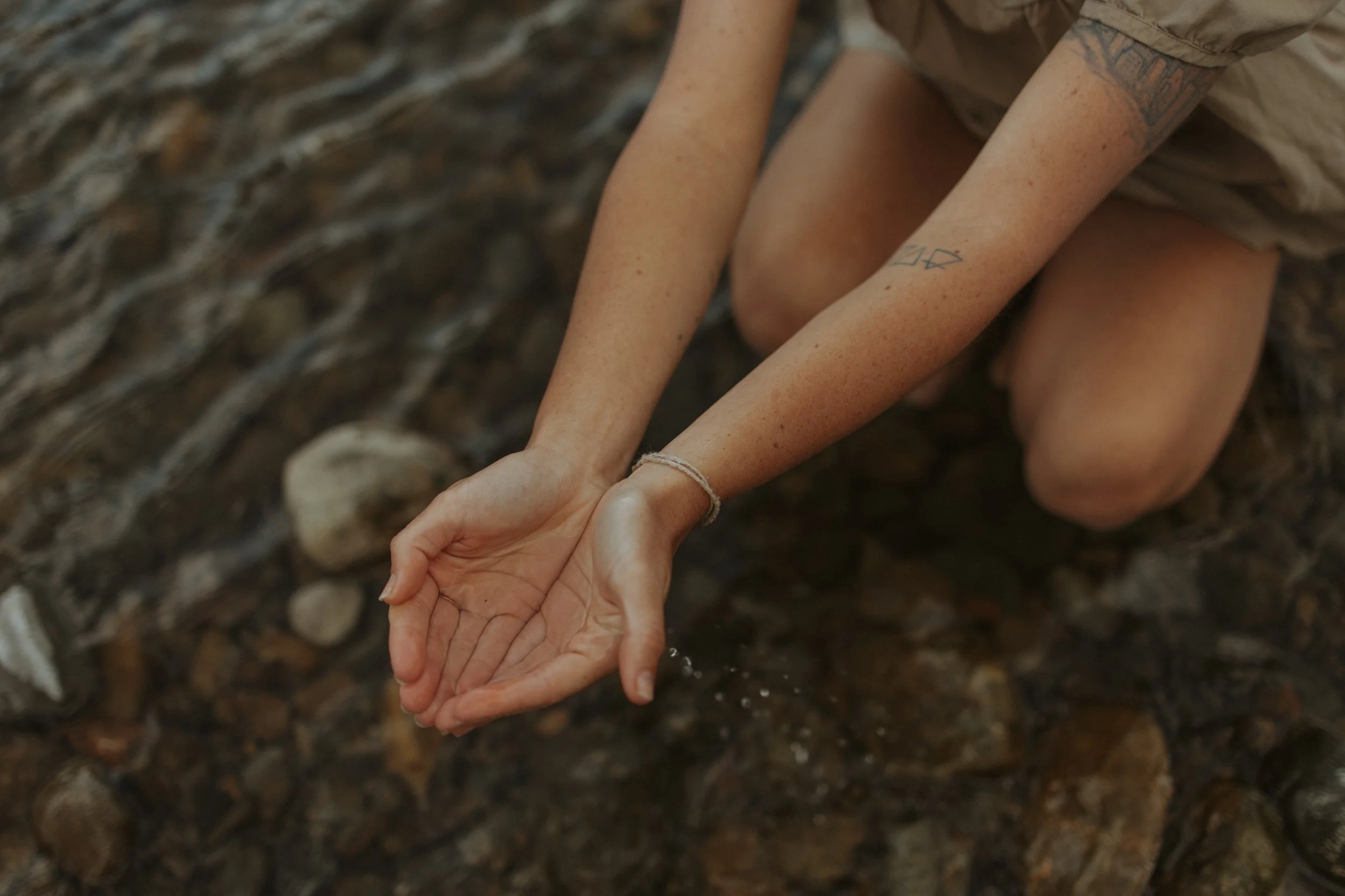 woman's hands holding water over a river