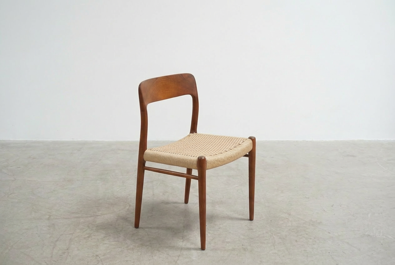 A wooden chair with a woven seat is placed in an empty room with plain white walls and a concrete floor.