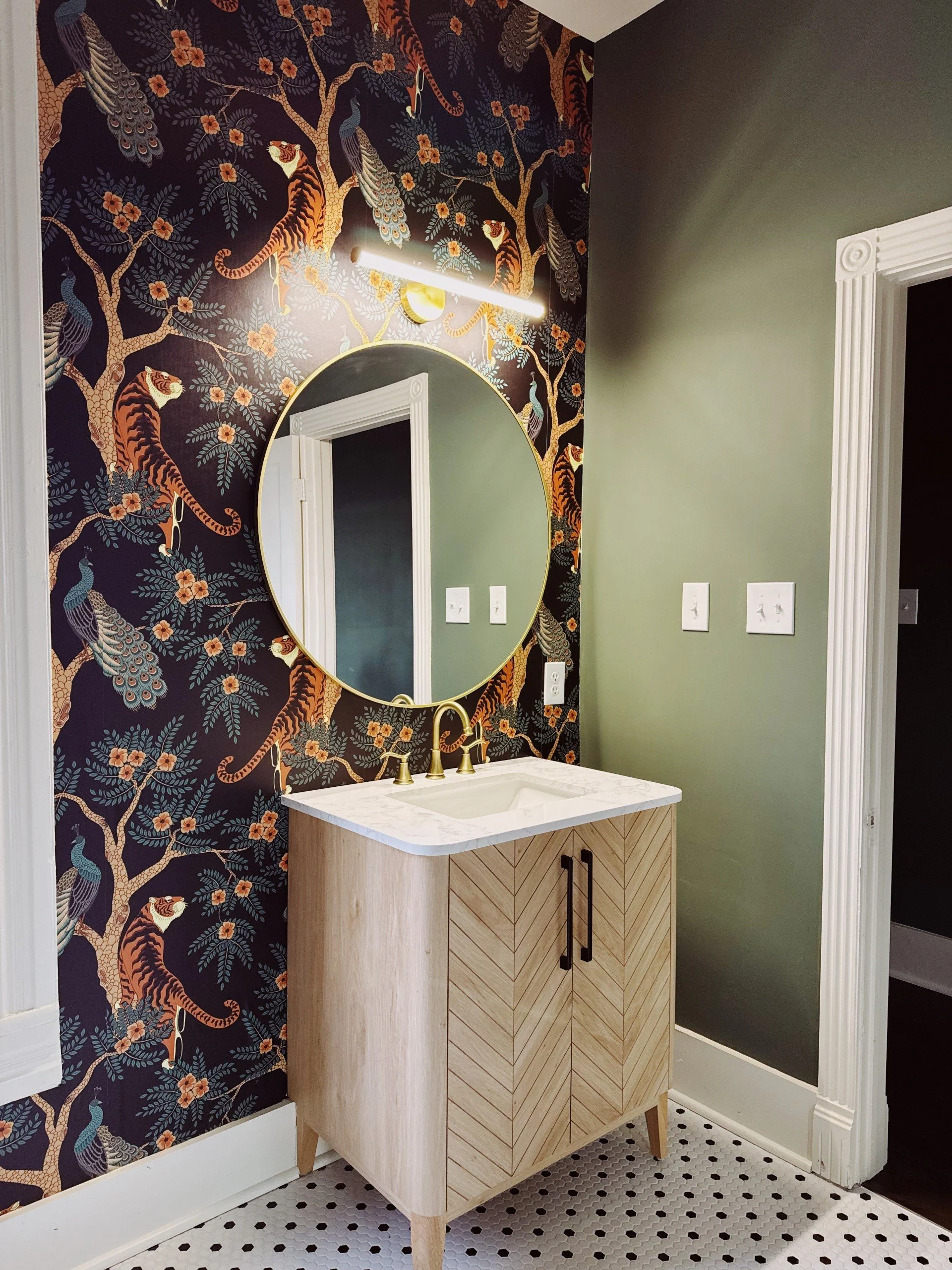 A bathroom with a vanity, round mirror, and a feature wall with tiger, peacock, and floral wallpaper.