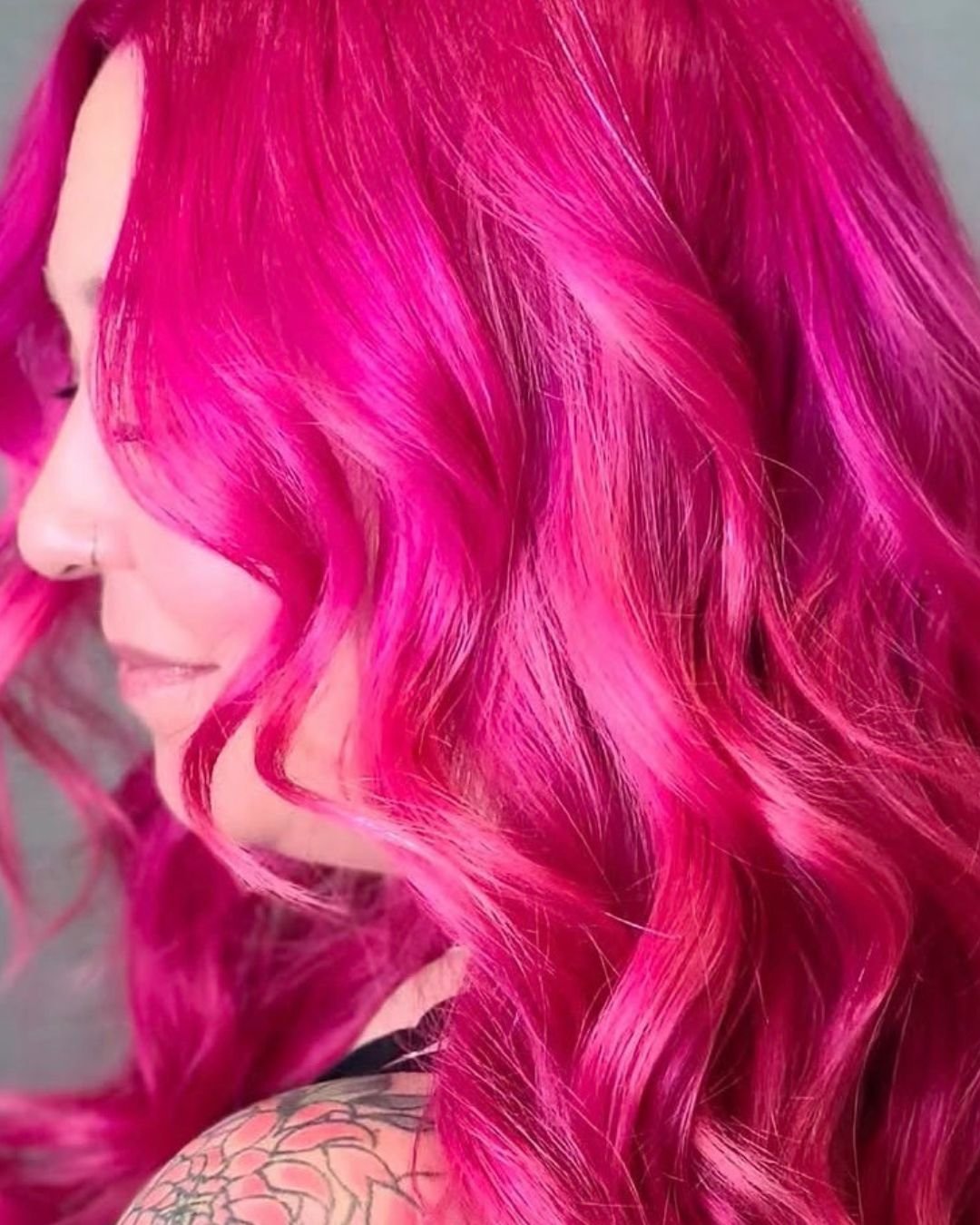 Close-up of a woman with vibrant bright pink, wavy hair.