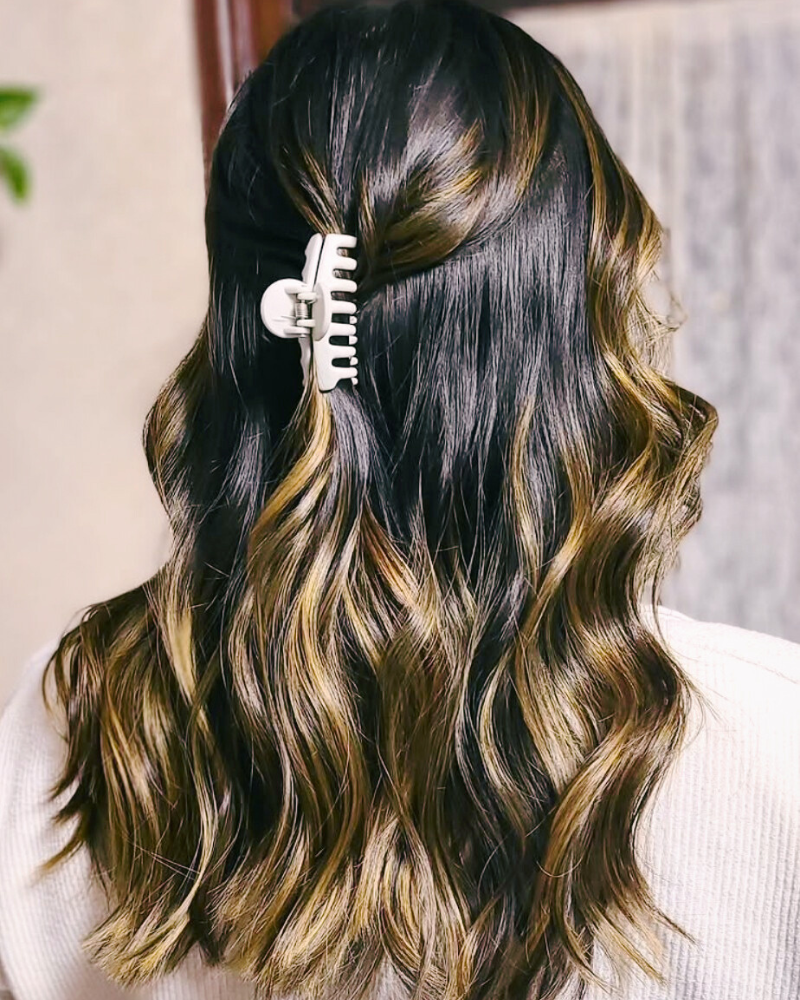 A person with wavy, dark brown hair with blonde highlights, partially clipped back with a large white hair clip.