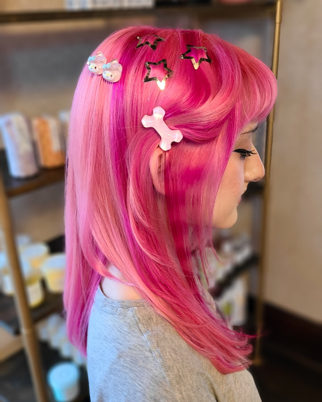 Side profile of woman with bright pink hair, adorned with colorful hair clips including puppy and star shapes, in a salon or hair studio.