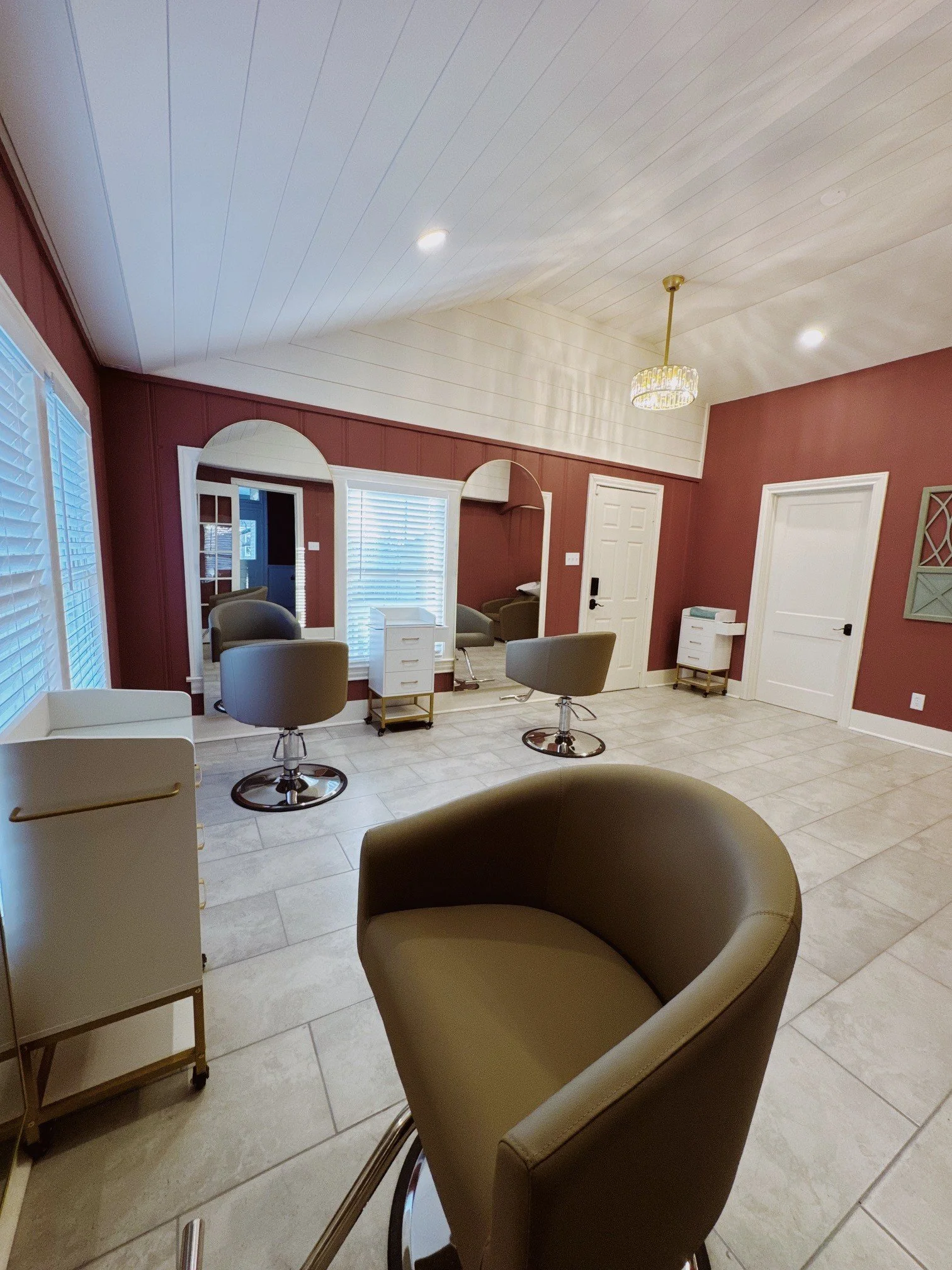 Interior of a hair salon with styling chairs, large mirrors, and a chandelier lighting fixture.