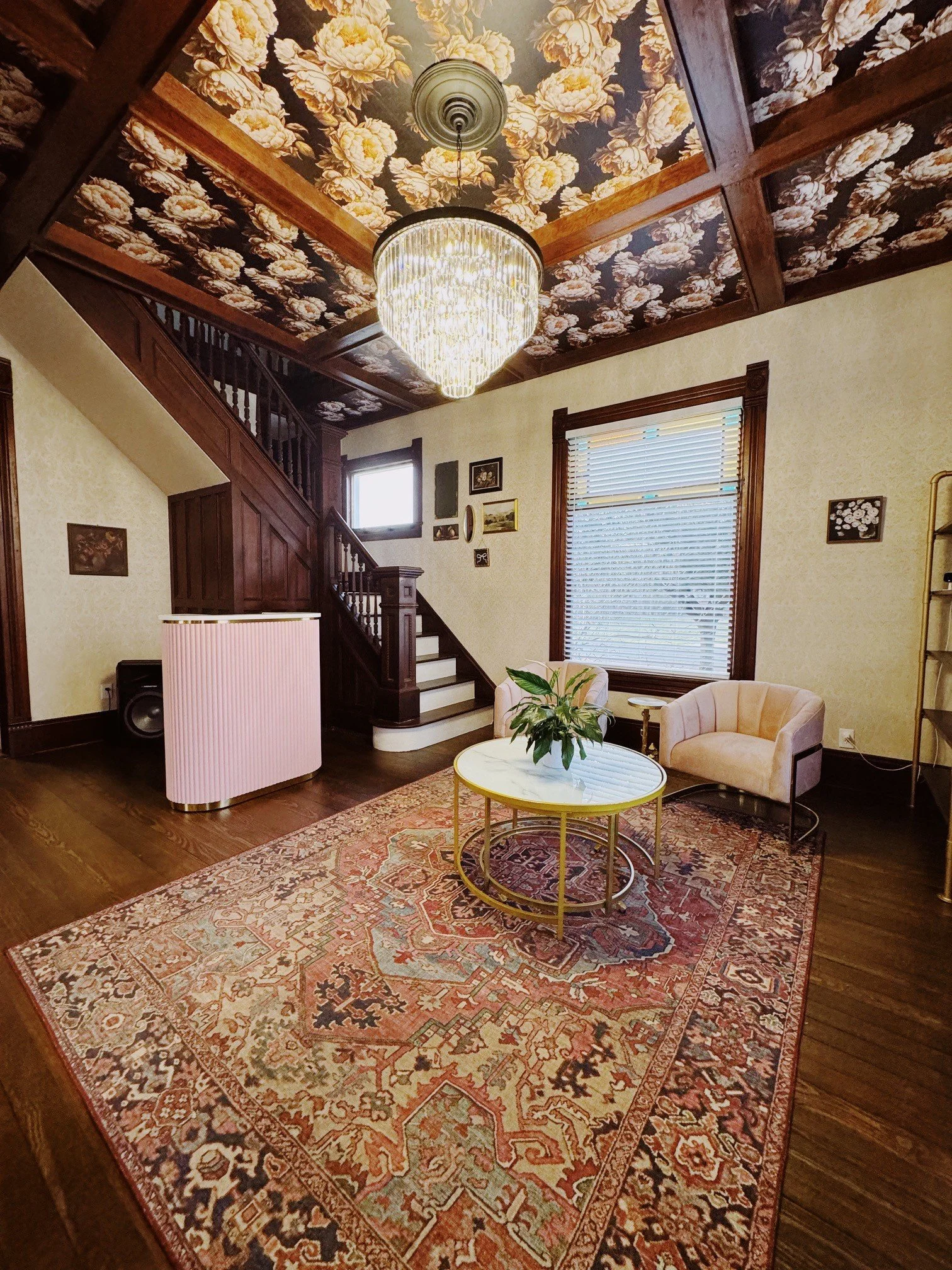 Living room with ornate floral ceiling, chandelier, beige half-circle armchair, pink radiator cover, and patterned area rug.