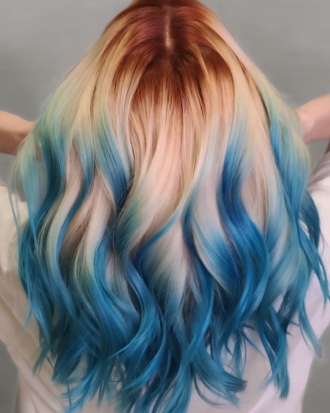 Person with long, wavy hair dyed in rainbow colors from pink and orange at the top, transitioning to yellow, green, light blue, and dark blue at the tips.