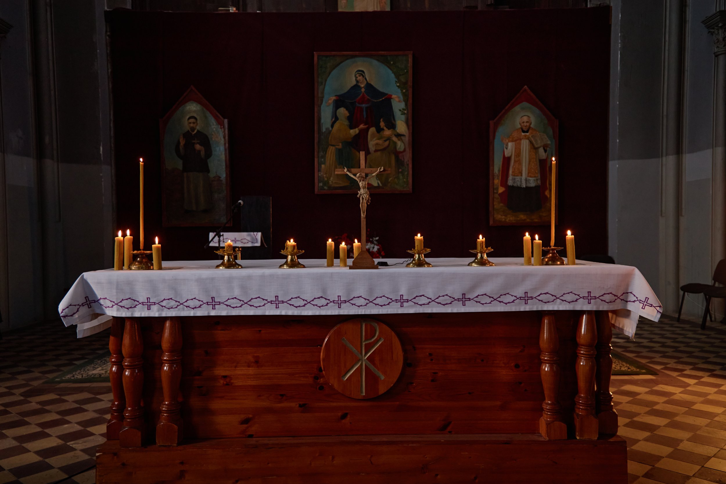 An altar in a church with lit candles, a crucifix, and religious paintings in the background.