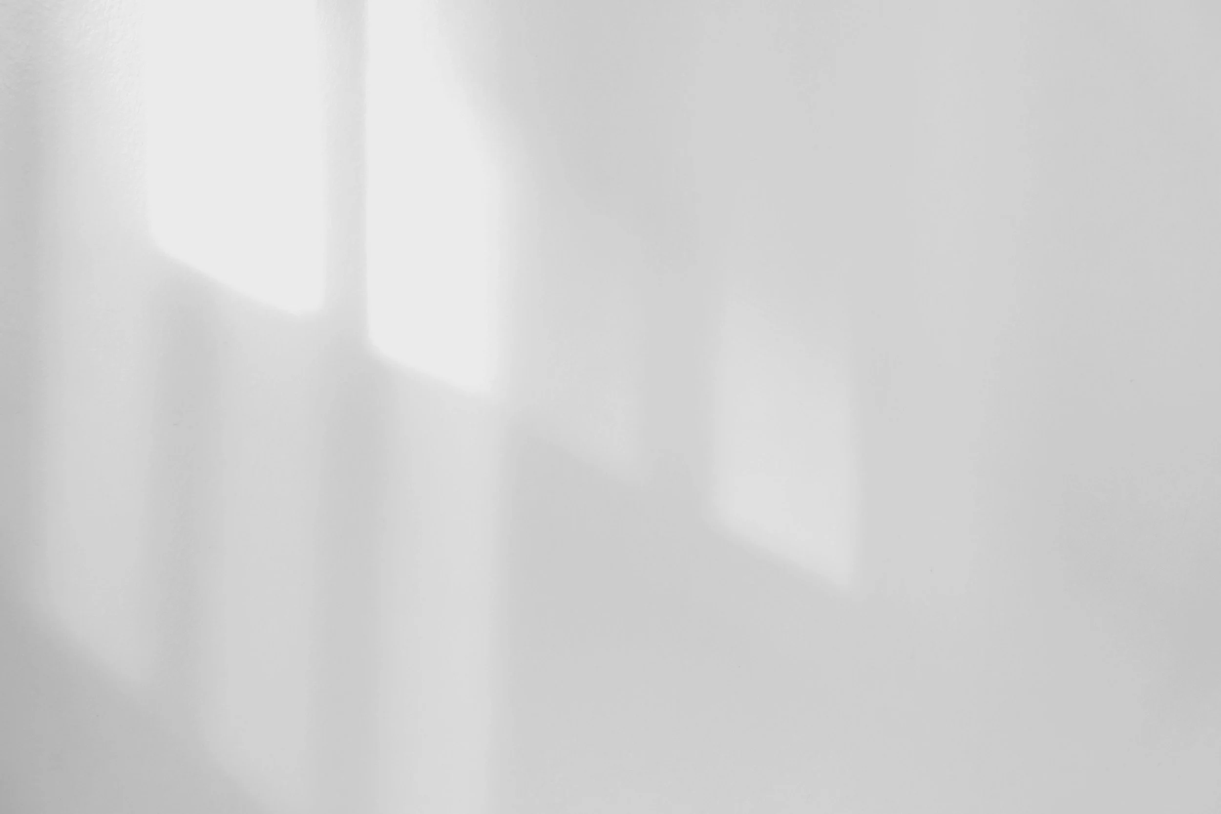 A blank white wall with sunlight casting a shadow of an open door or window.