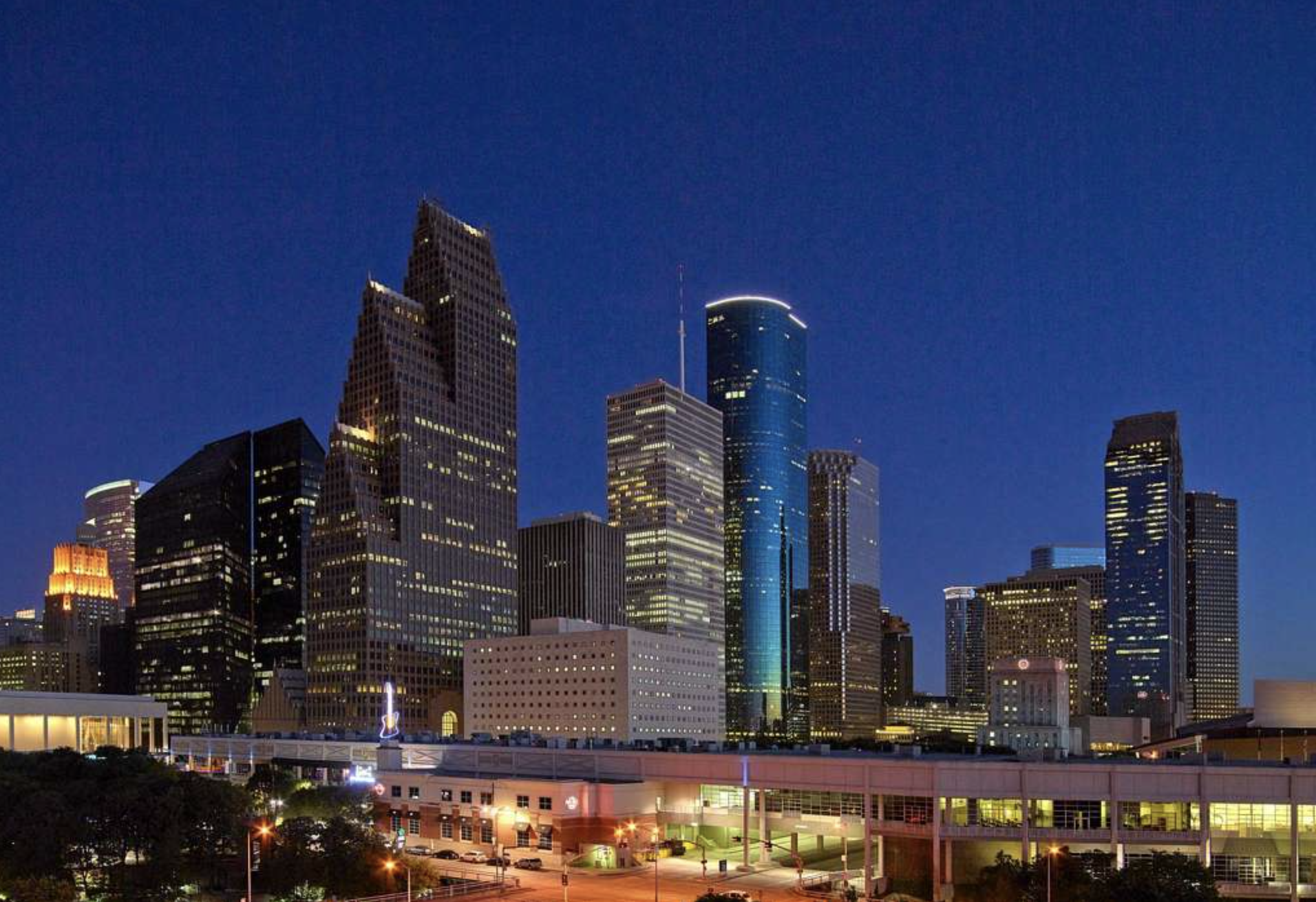 Nighttime city skyline of downtown Dallas, Texas with illuminated skyscrapers and blue evening sky.