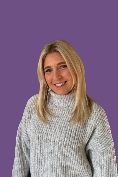 A woman with blonde hair wearing a warm turtleneck sweater, smiling against a purple background.