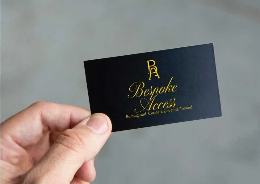 A hand holding a black business card with gold text that reads "A Bespoke Access" and the tagline "Reimagined. Curated. Elevated. Trusted."