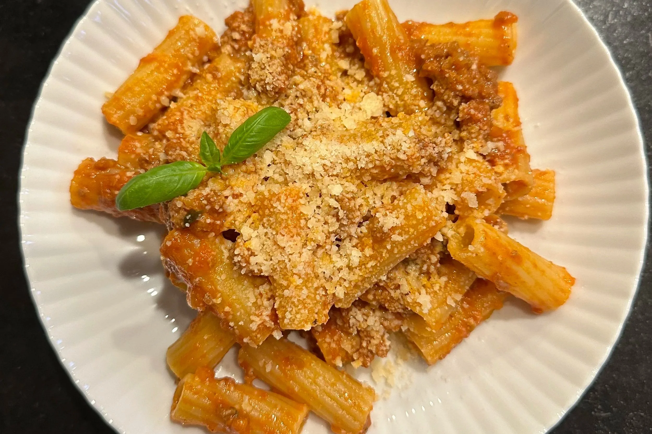 Plate of baked rigatoni pasta topped with tomato sauce, grated cheese, and fresh basil leaves.