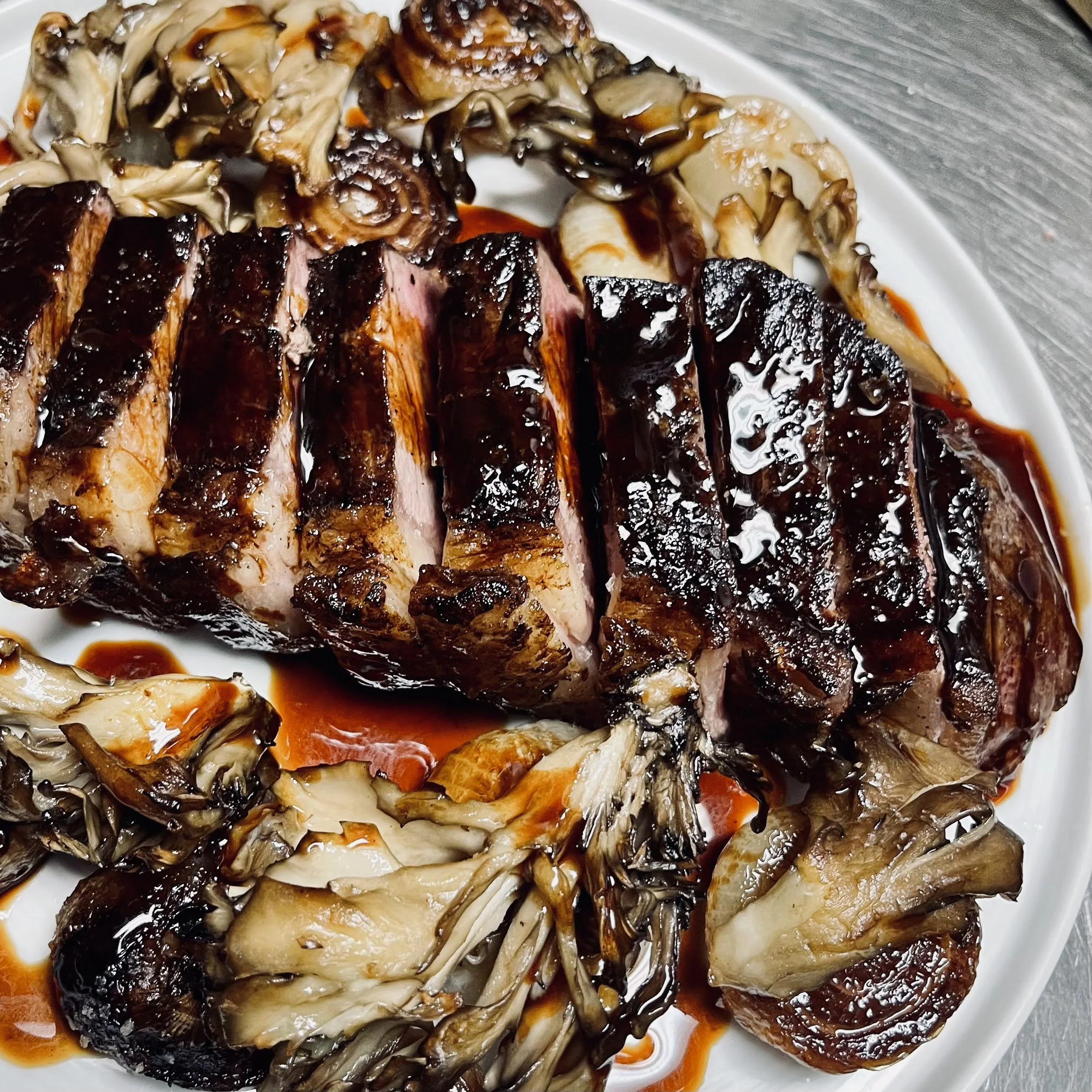 Slices of cooked steak with a dark glaze, garnished with mushrooms on a white plate.