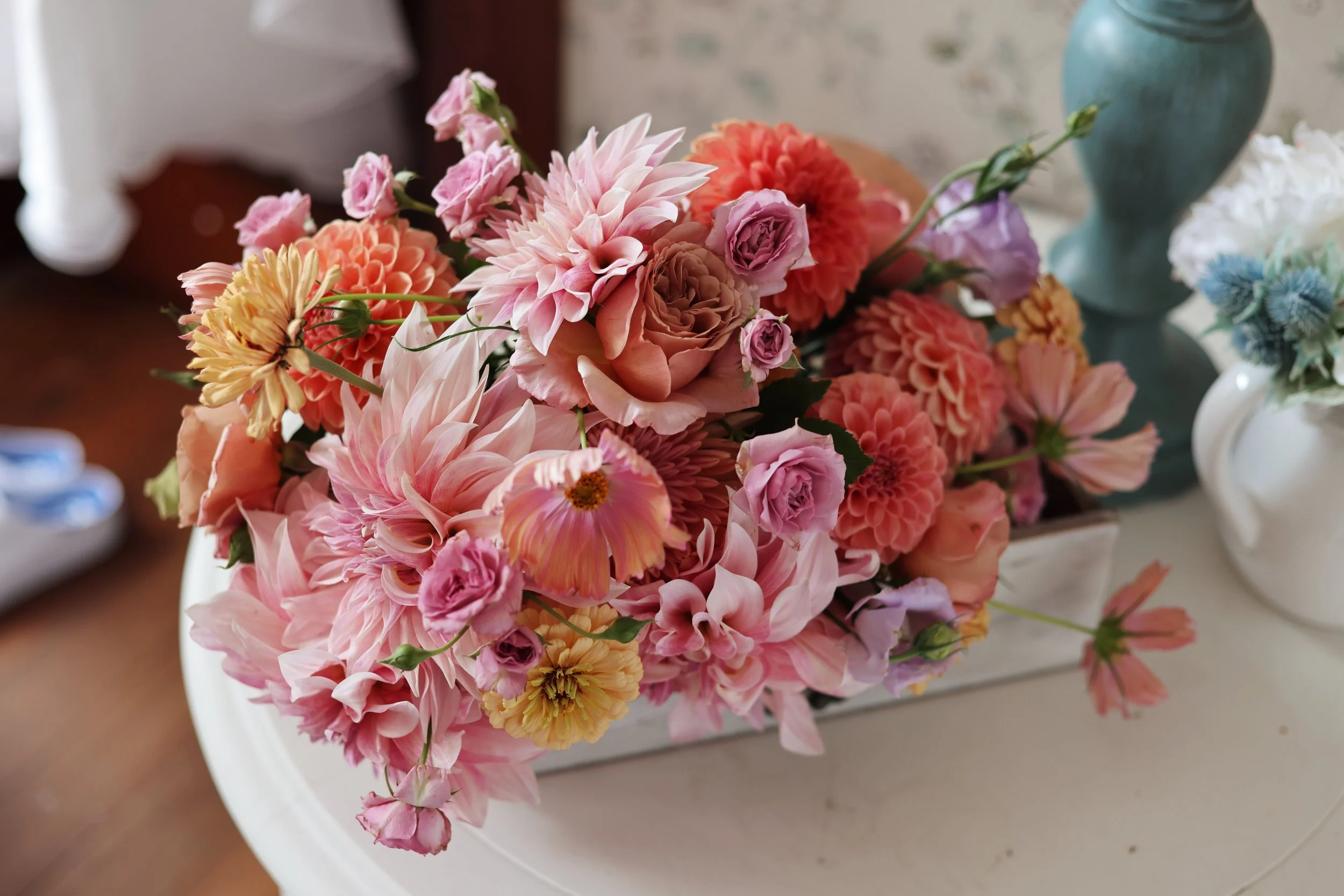 A colorful bouquet of pink, peach, yellow, and lavender flowers in a white rectangular vase on a white table.
