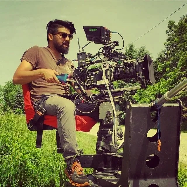 Man operating a professional film camera outdoors in a green grassy area.