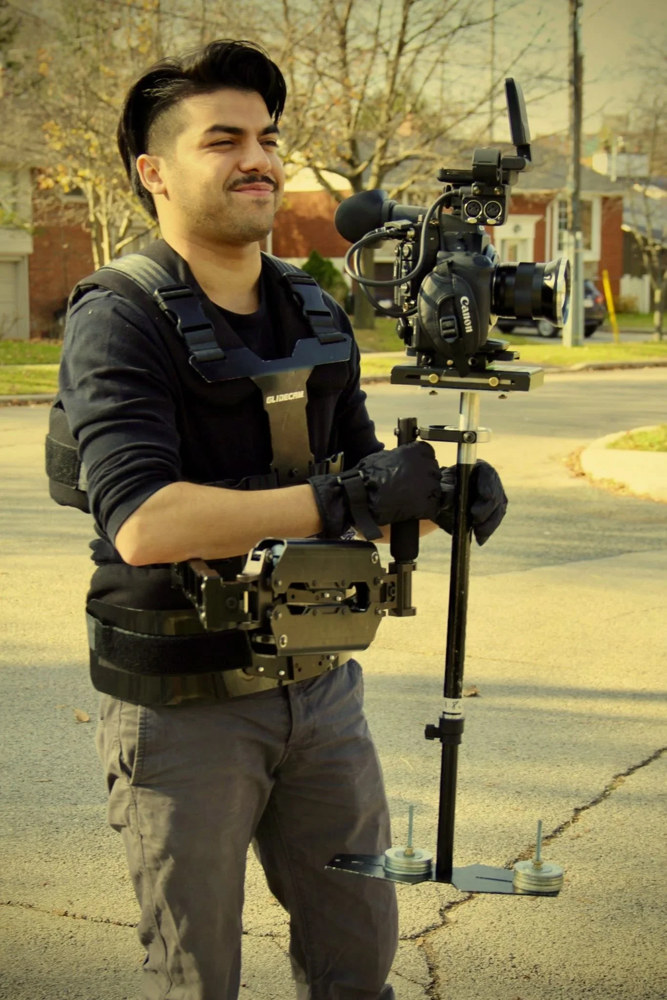 A young man operating a camera on a stabilizer rig outdoors in a residential neighborhood.