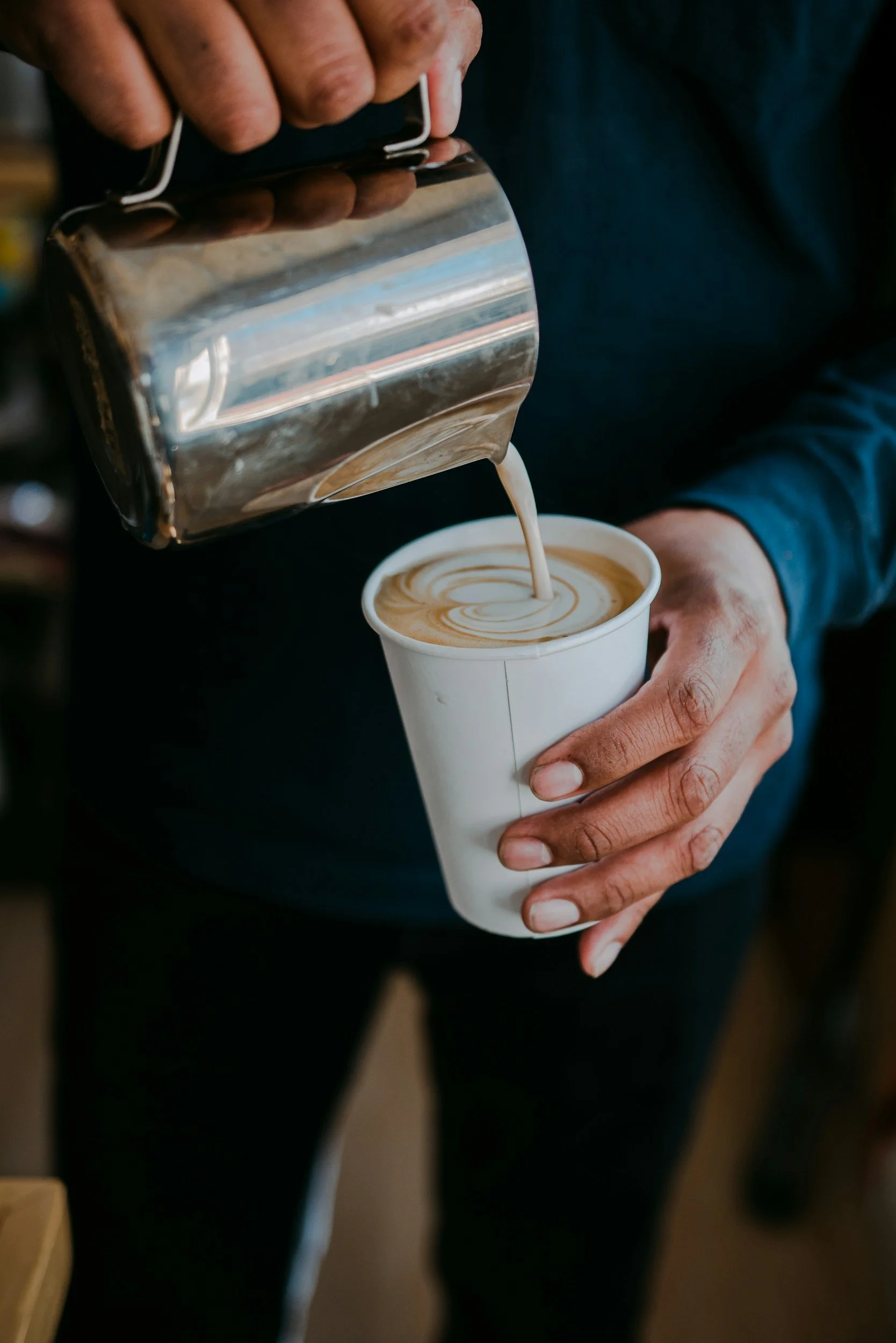 A person pouring steamed milk into a paper cup to make a latte.
