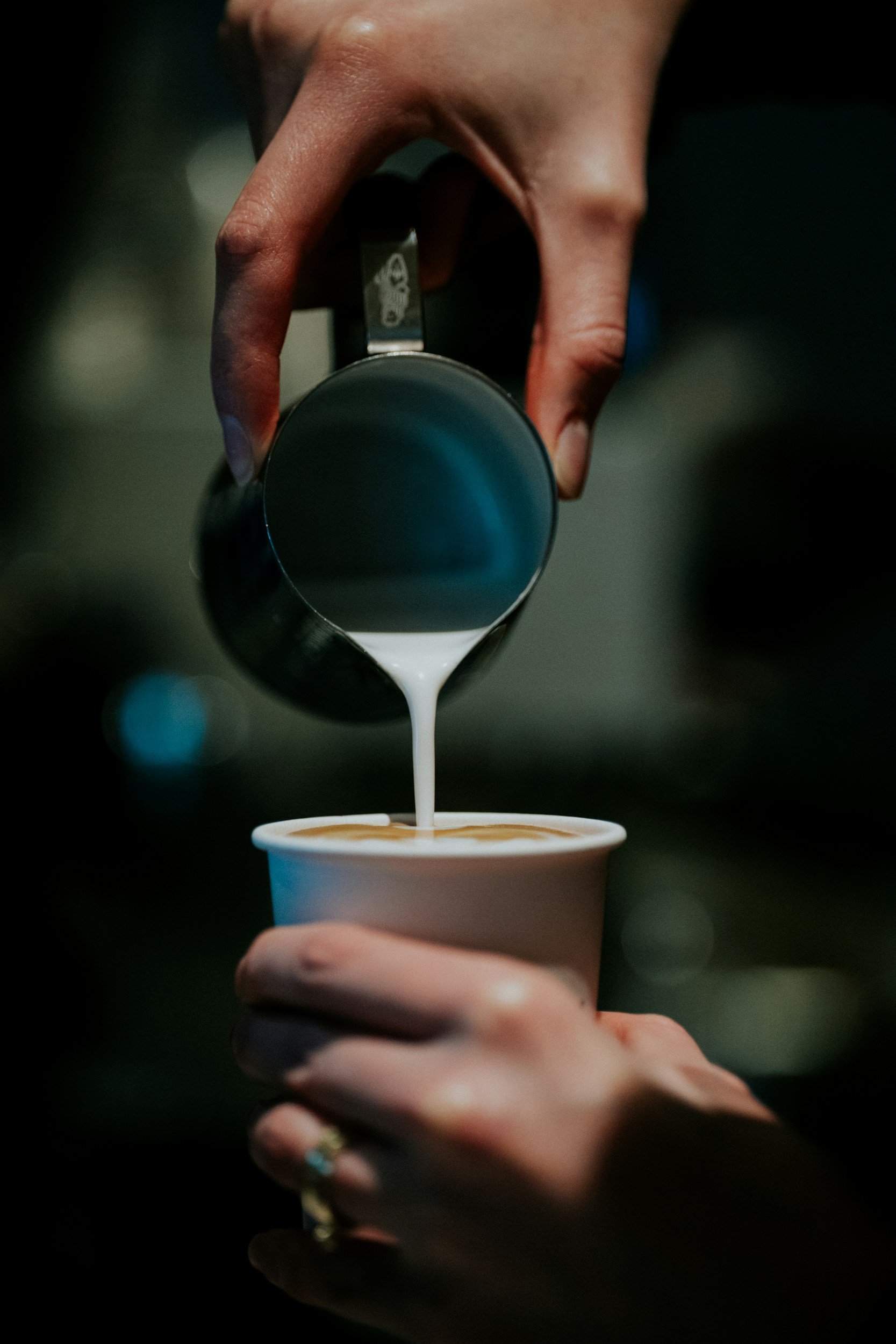 Person pouring milk into a cup of coffee.