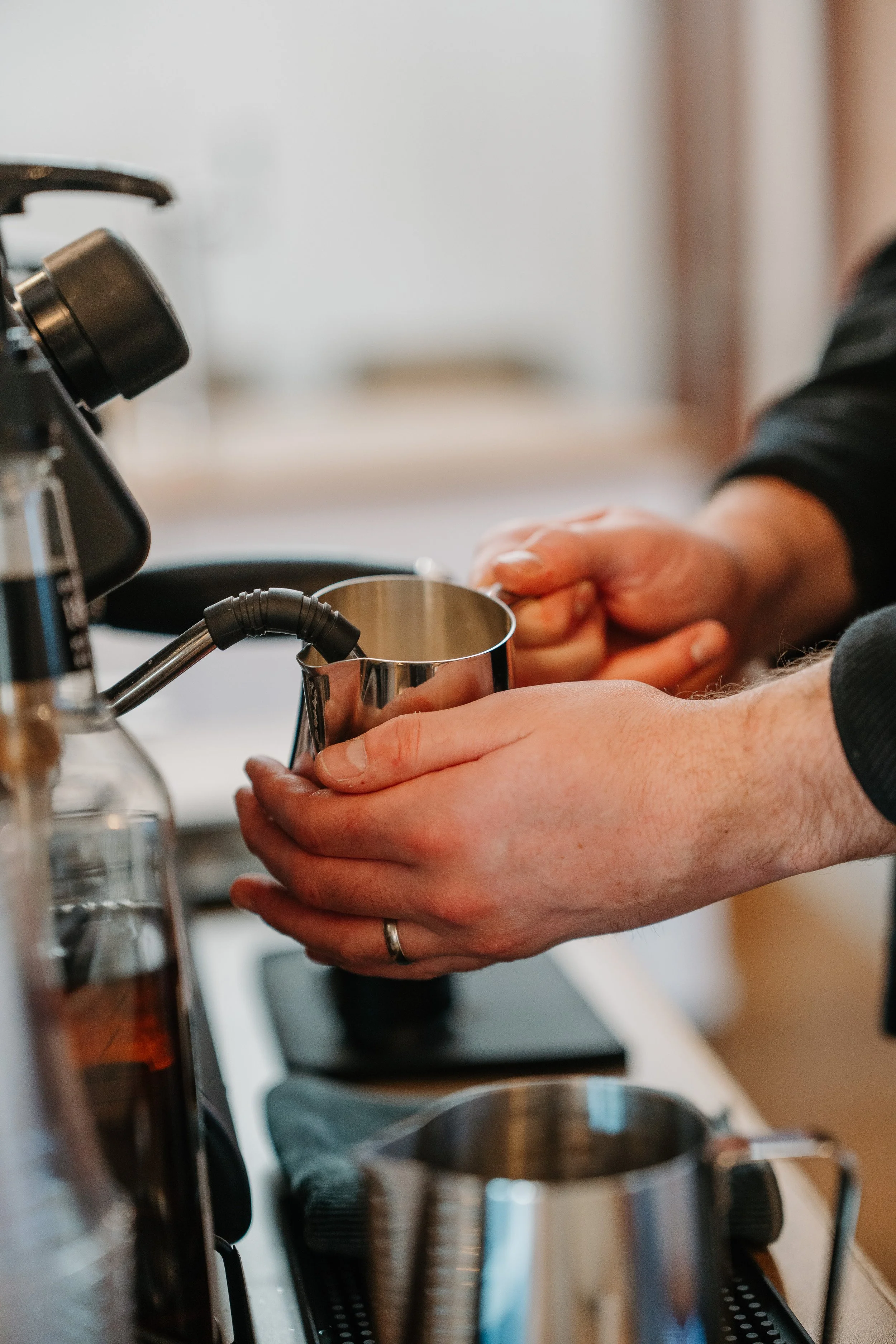 barista steaming milk in a pitcher with espresso machine frother