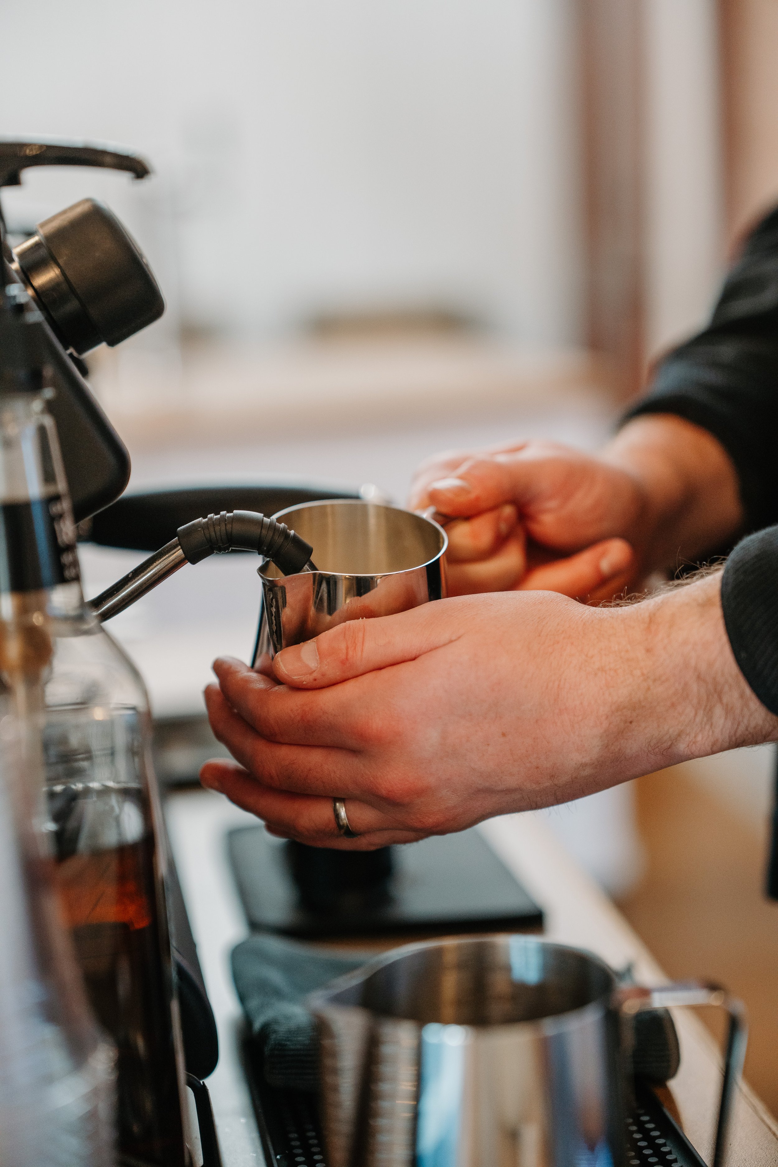 Barista holding a milk pitcher while steaming the milk