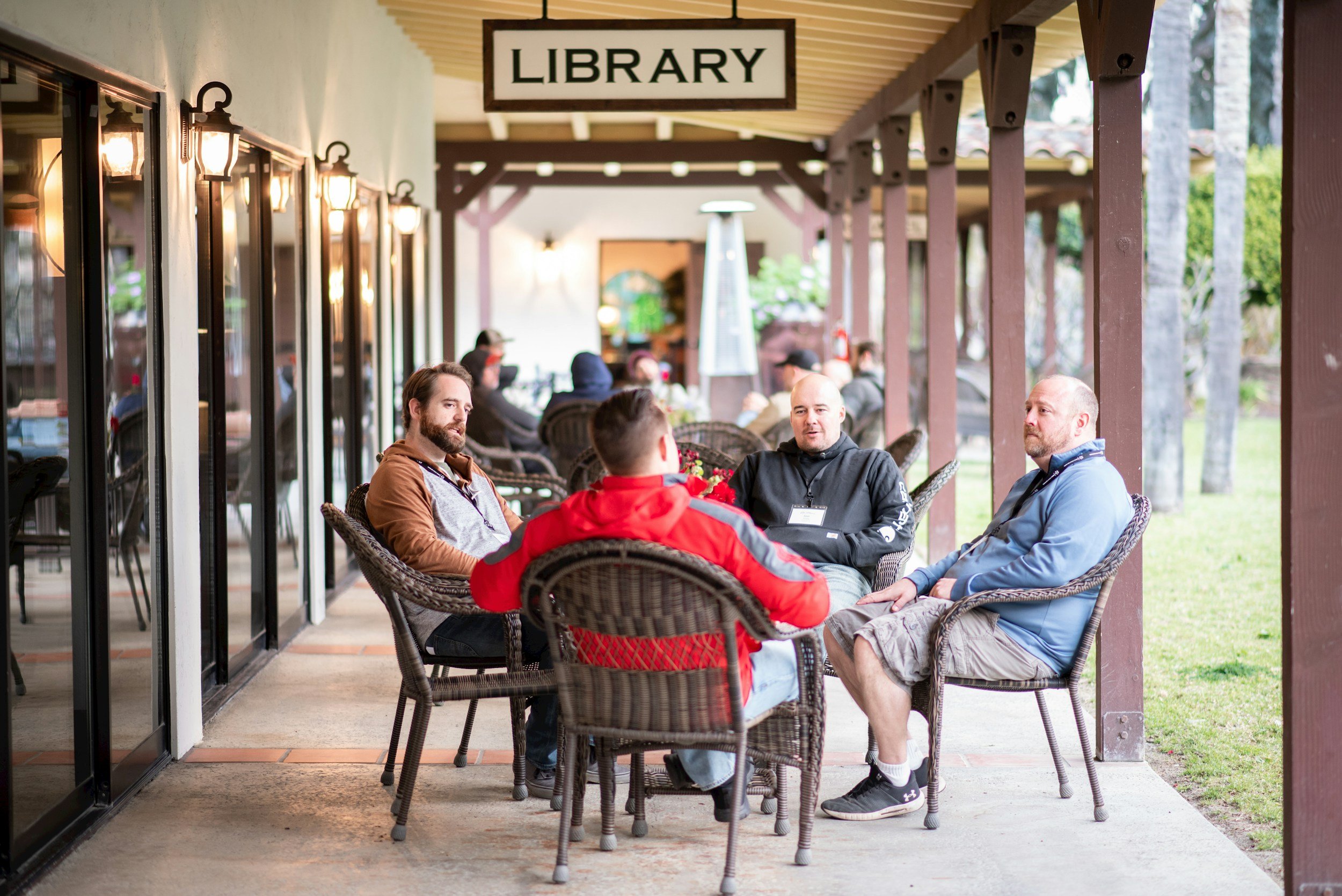 Group of five men sitting on wicker chairs having a conversation on the outdoors patio of a library. Steve Osborne, PhD, Beyond Chance