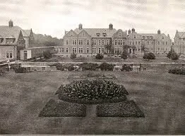 A large historic estate or mansion with grand architecture, surrounded by a well-manicured lawn and gardens.