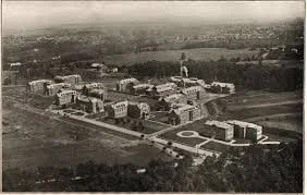 Aerial view of a college campus with multiple buildings and a courtyard, surrounded by open land.