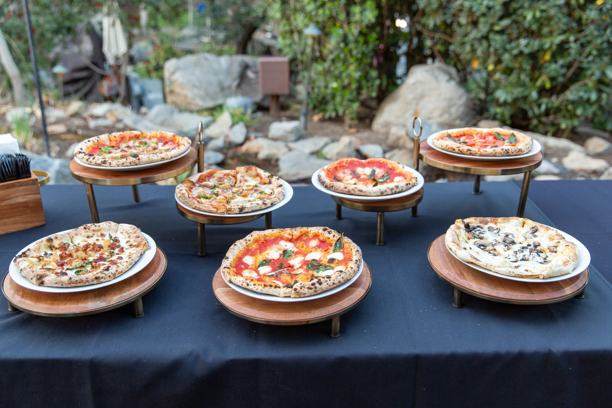 Wood-fired pizzas displayed on serving stands at an Olive Wood Pizza catering event