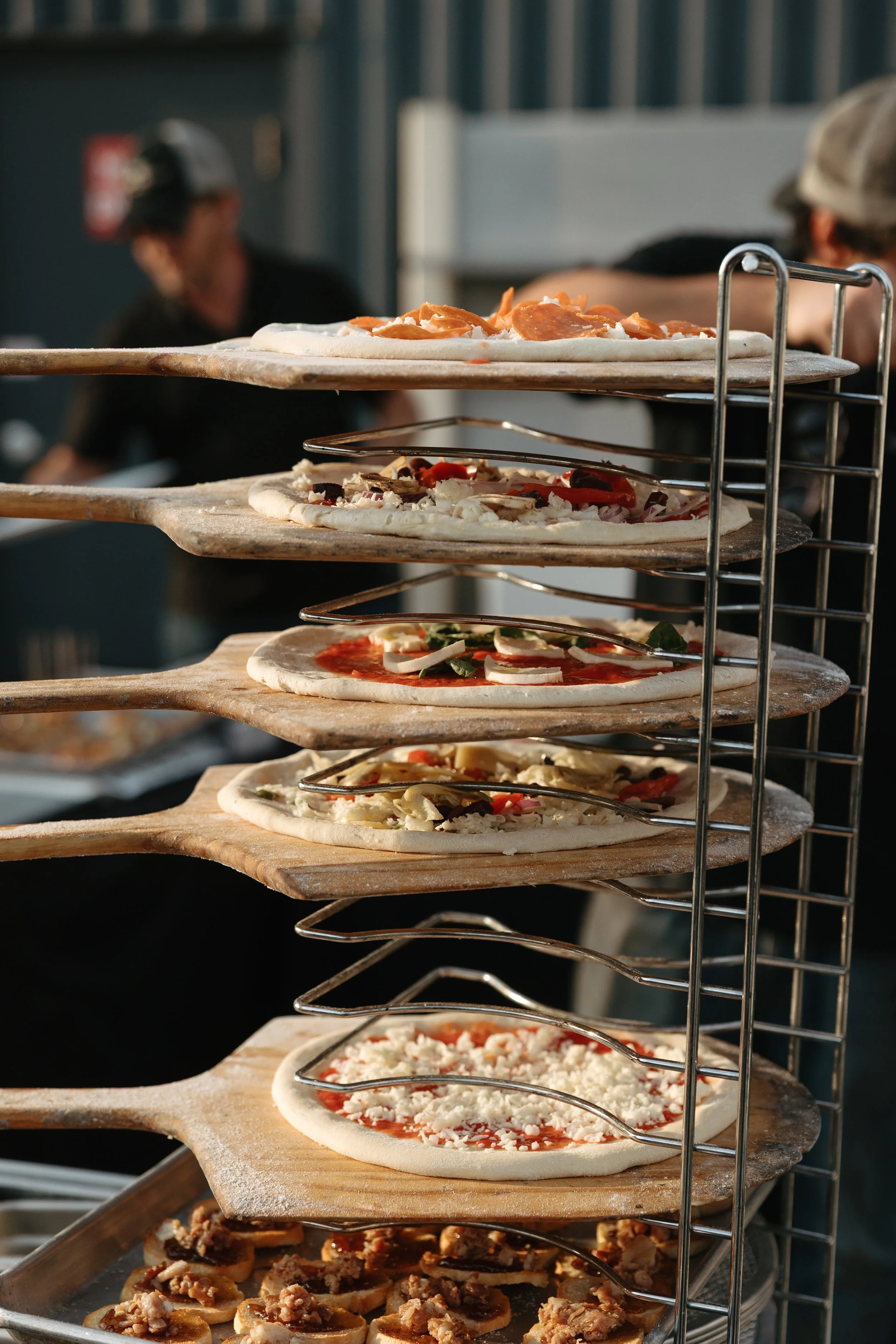 Freshly prepared pizzas on wooden peels ready for baking at an Olive Wood Pizza event