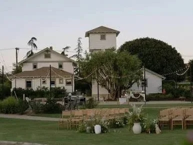 Outdoor scene at the Swanner House in San Juan Capistrano with houses, trees, a well-manicured lawn, chairs, and large white vases.