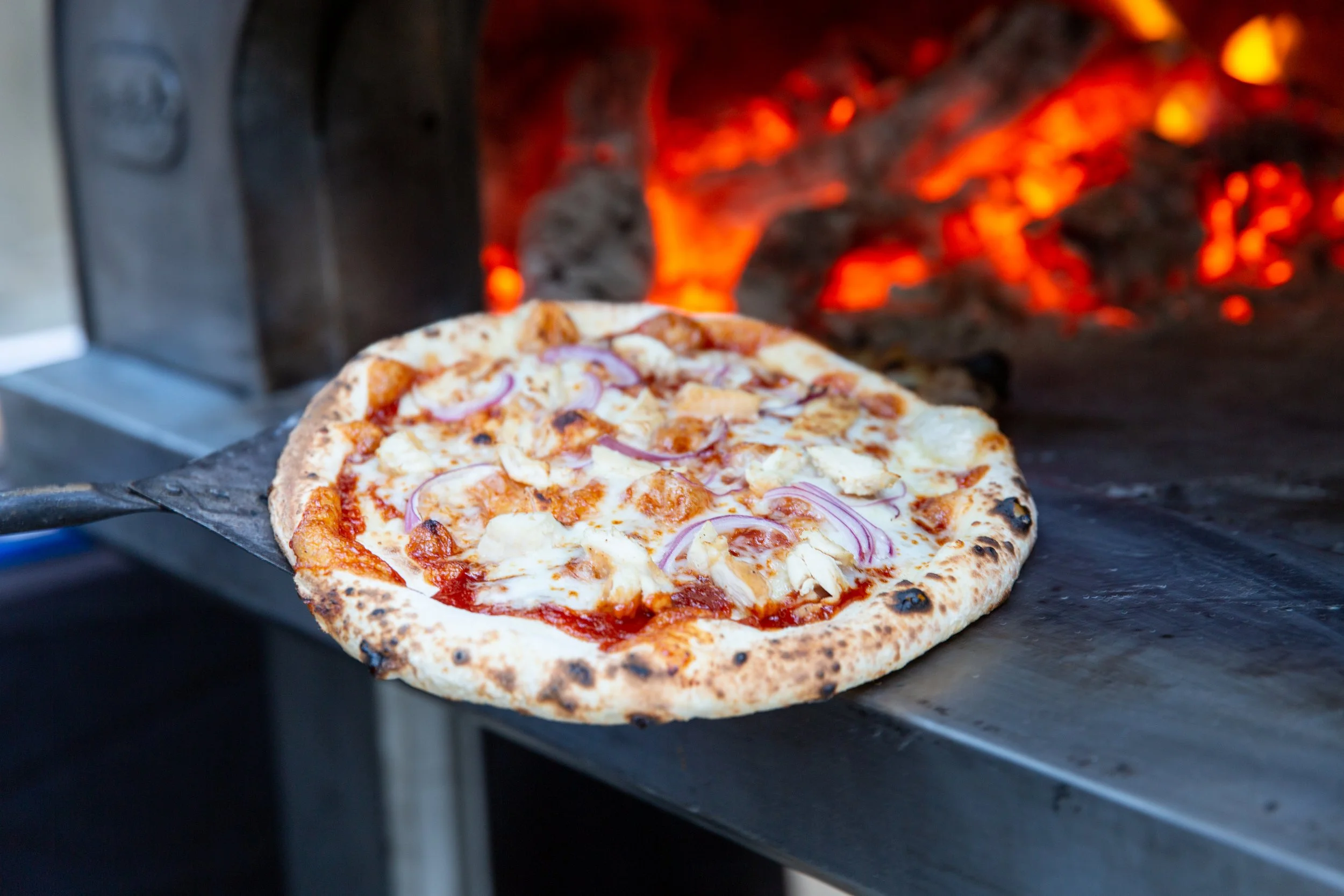 Wood-fired pizza cooking in an olive wood oven at an Olive Wood Pizza event