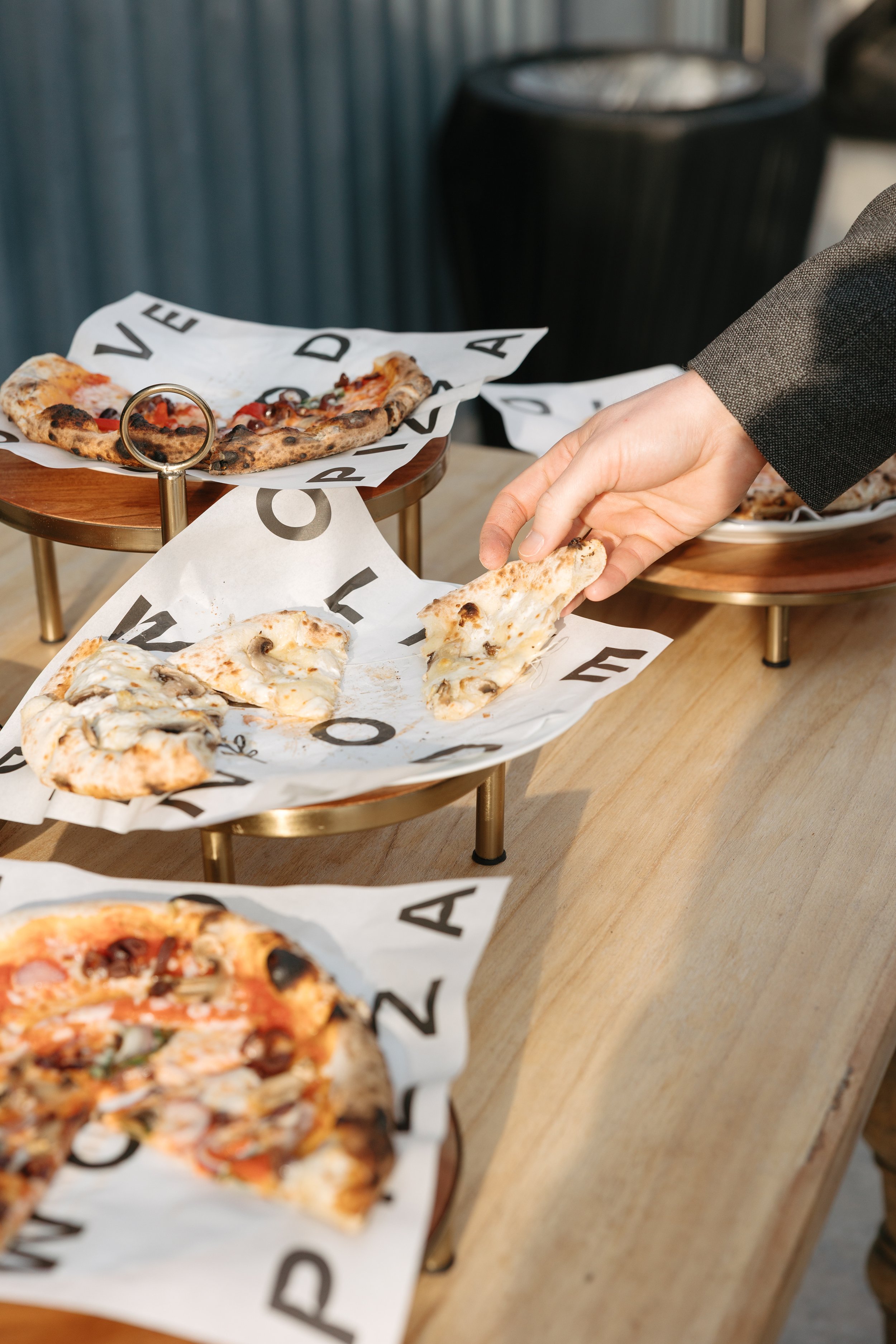 Guest taking a slice of wood-fired pizza from a display at an Olive Wood Pizza catered event