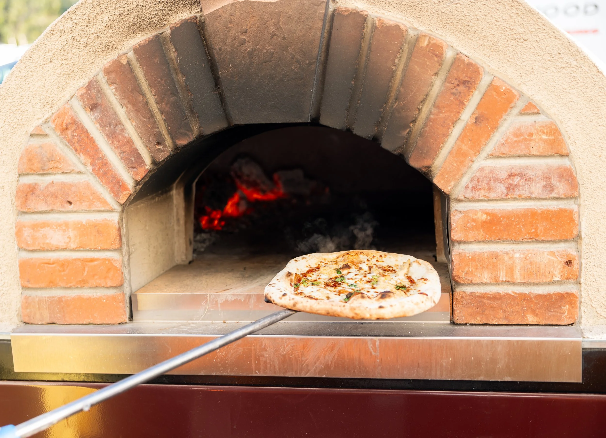 Wood-fired pizza baking in an olive wood oven at an Olive Wood Pizza catered event