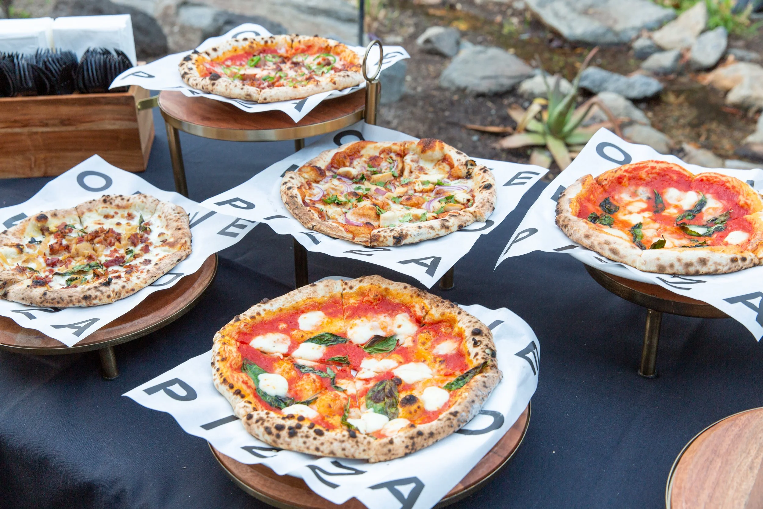 Assorted Olive Wood Pizza wood-fired pizzas displayed at a catered event.