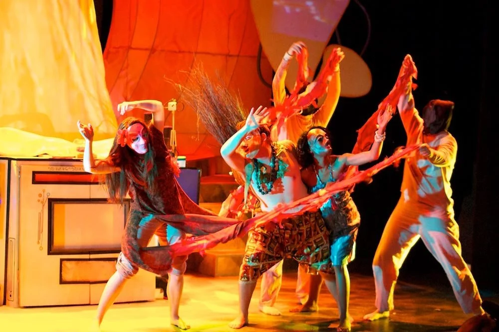 Performance with multiple dancers on stage, colorful costumes, expressive poses, and vibrant lighting.