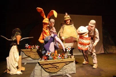 Children in animal and costume masks performing a puppet show on stage.