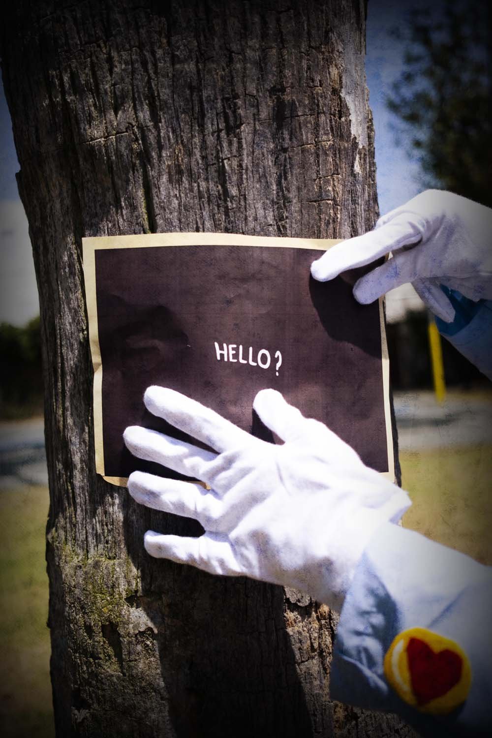 Person wearing white gloves placing a note on a tree that says 'HELLO?'