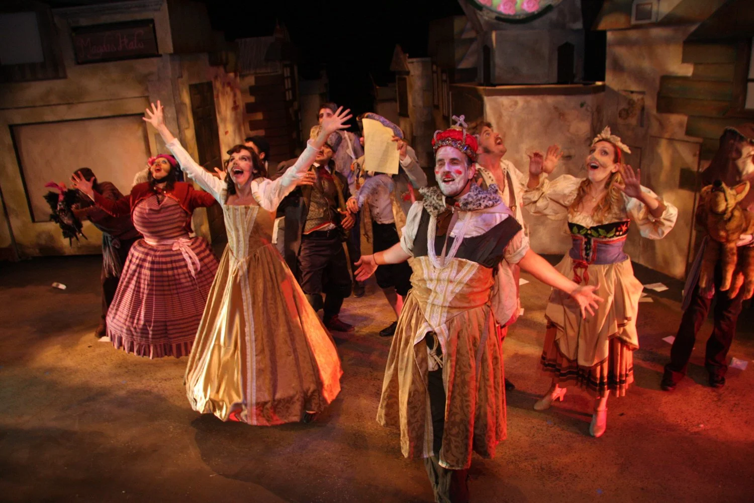 Actors performing on stage in a musical or theatrical production, dressed in period costumes resembling 18th-century European attire, with expressive gestures and joyful expressions.