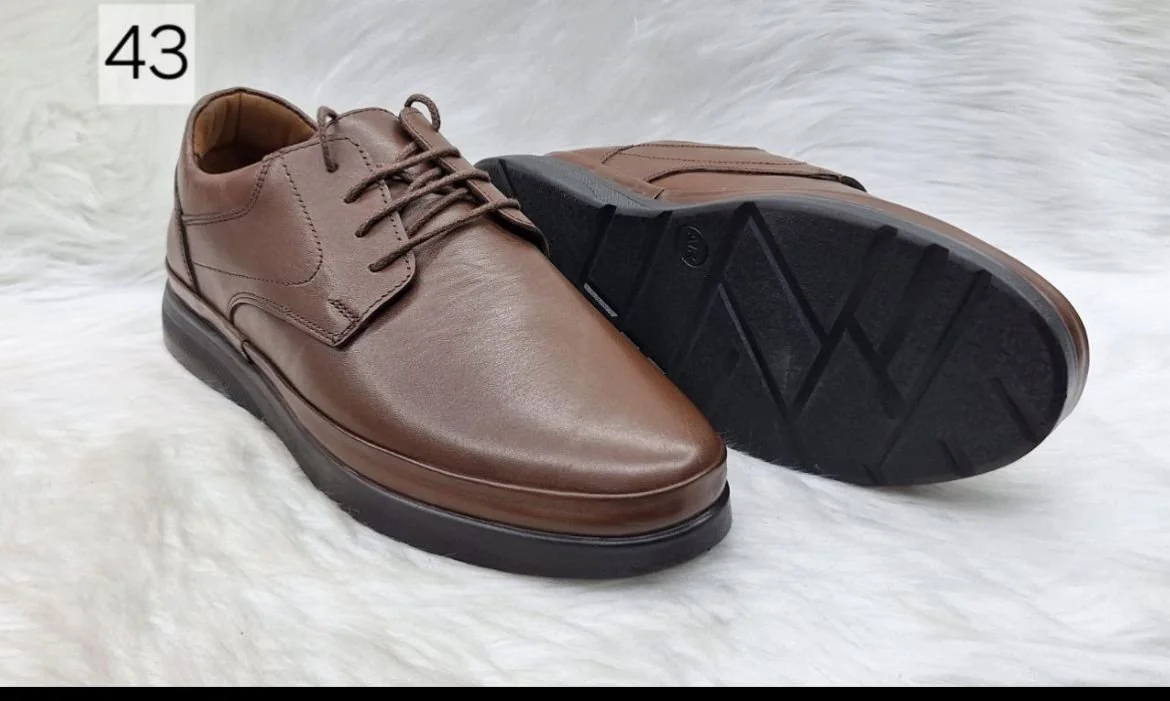 Pair of brown leather dress shoes with black soles, placed on a white fuzzy surface.