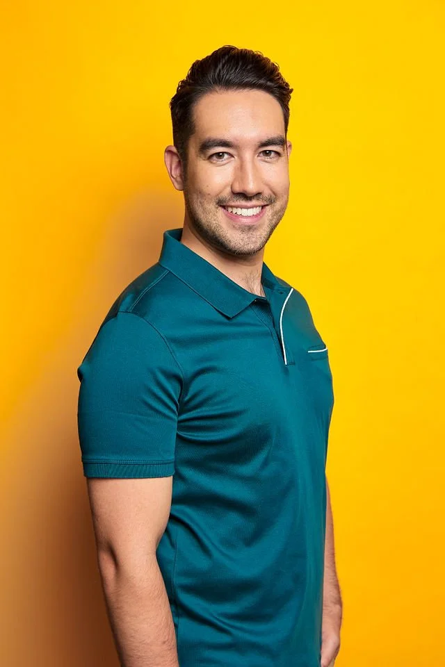 Taylor Hurst commercial model and professional actor smiling in a teal polo shirt against a yellow background, perfect for lifestyle, dad, or tech-related campaigns.