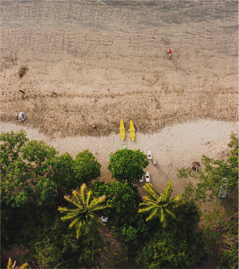 Aerial view of a beach with three yellow kayaks on the sand, some trees at the bottom, and a few people scattered on the sand.