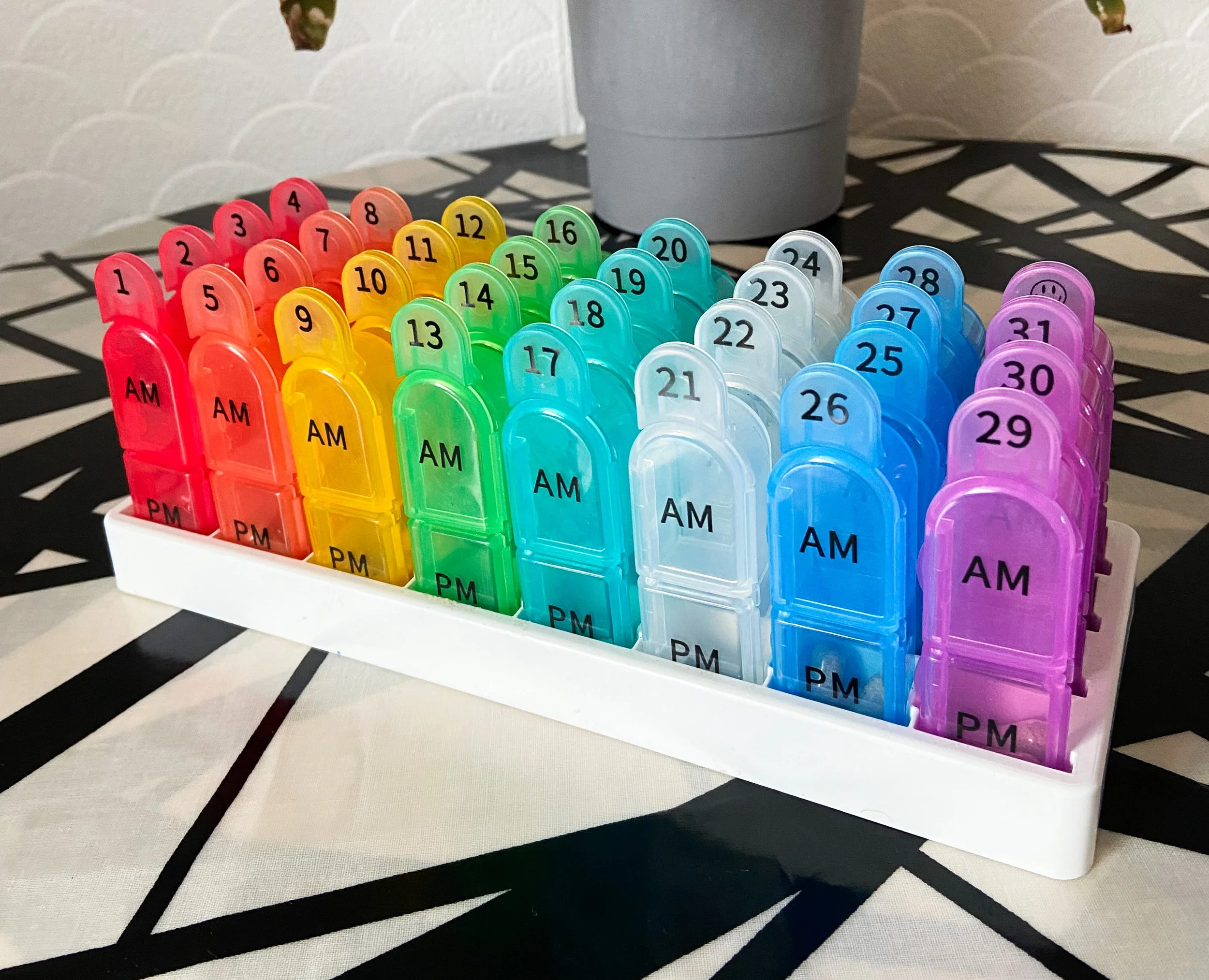 Close up of a monthly refillable dosset box in a holder for adhd medication organisation. There are individual boxes each with a number to indicate the date. On a zig zagged table cloth.